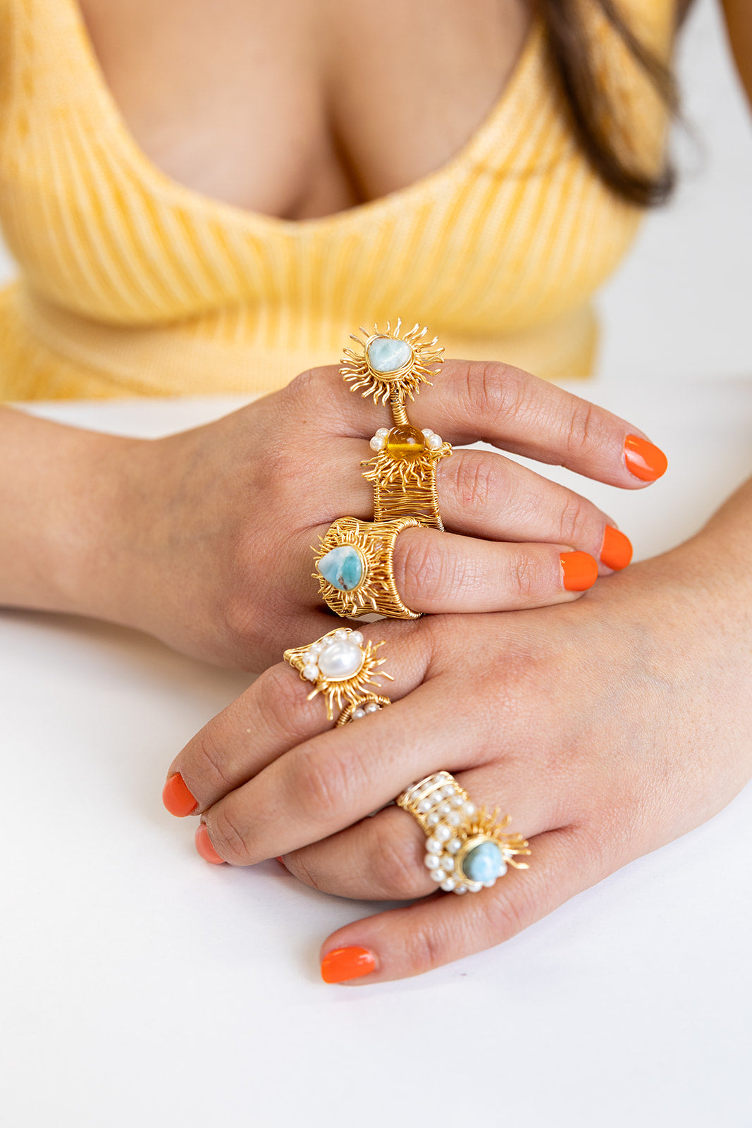Close-up of hands wearing gold rings with Larimar stones and freshwater pearls on a white background