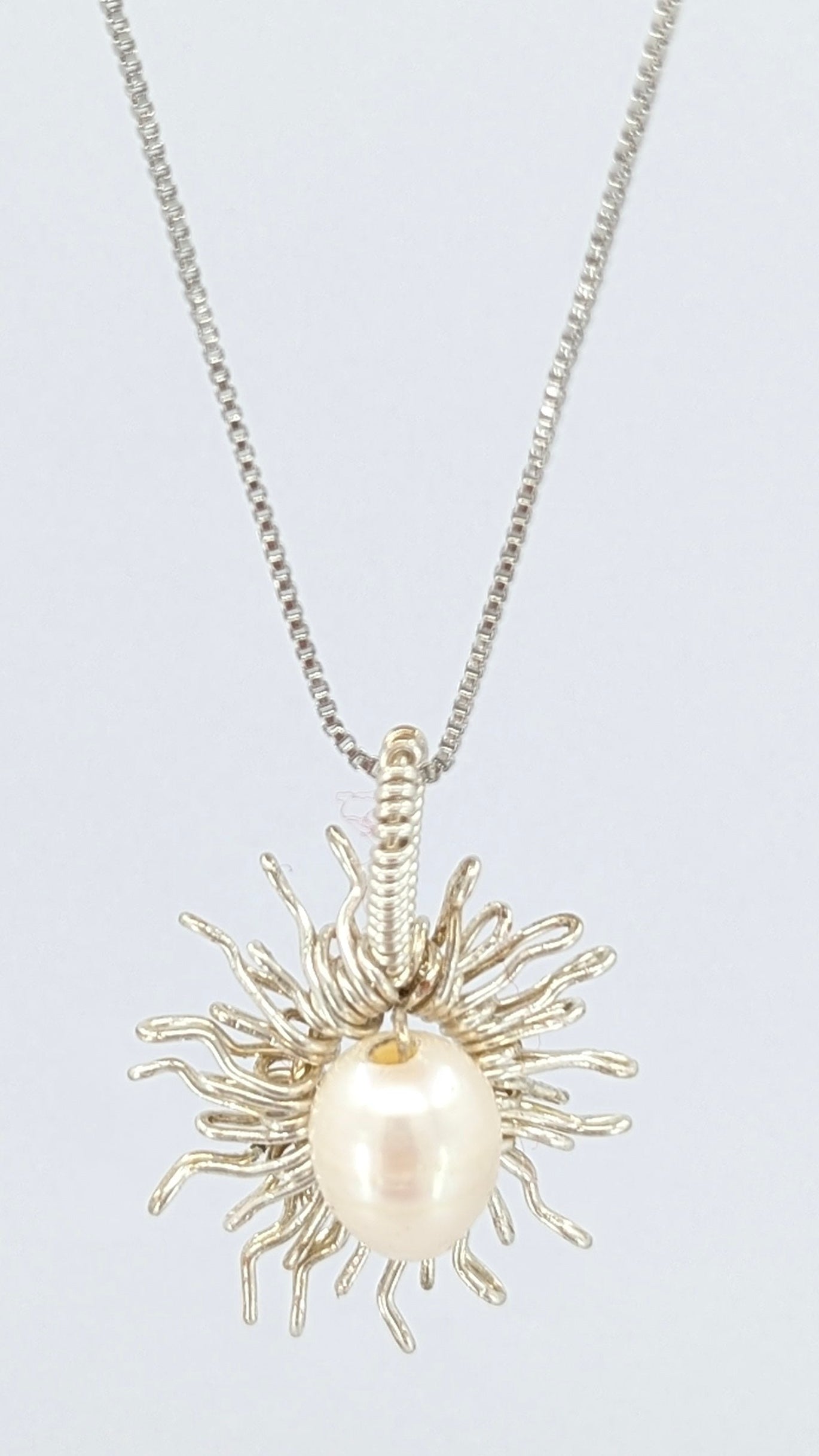 Front view of Necklace with a sun-shaped pendant featuring a freshwater pearl on a light gray background.