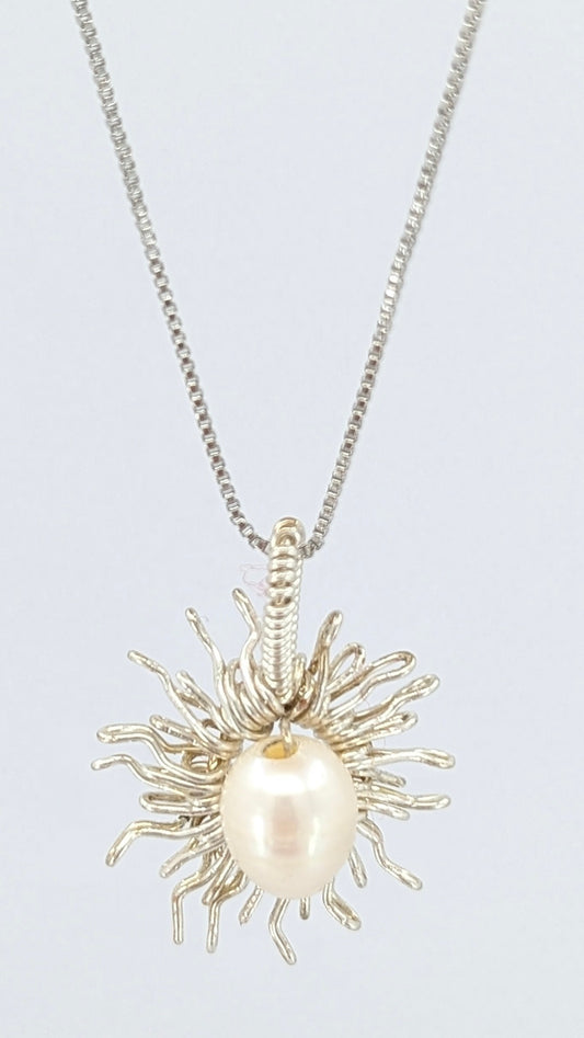 Front view of Necklace with a sun-shaped pendant featuring a freshwater pearl on a light gray background.