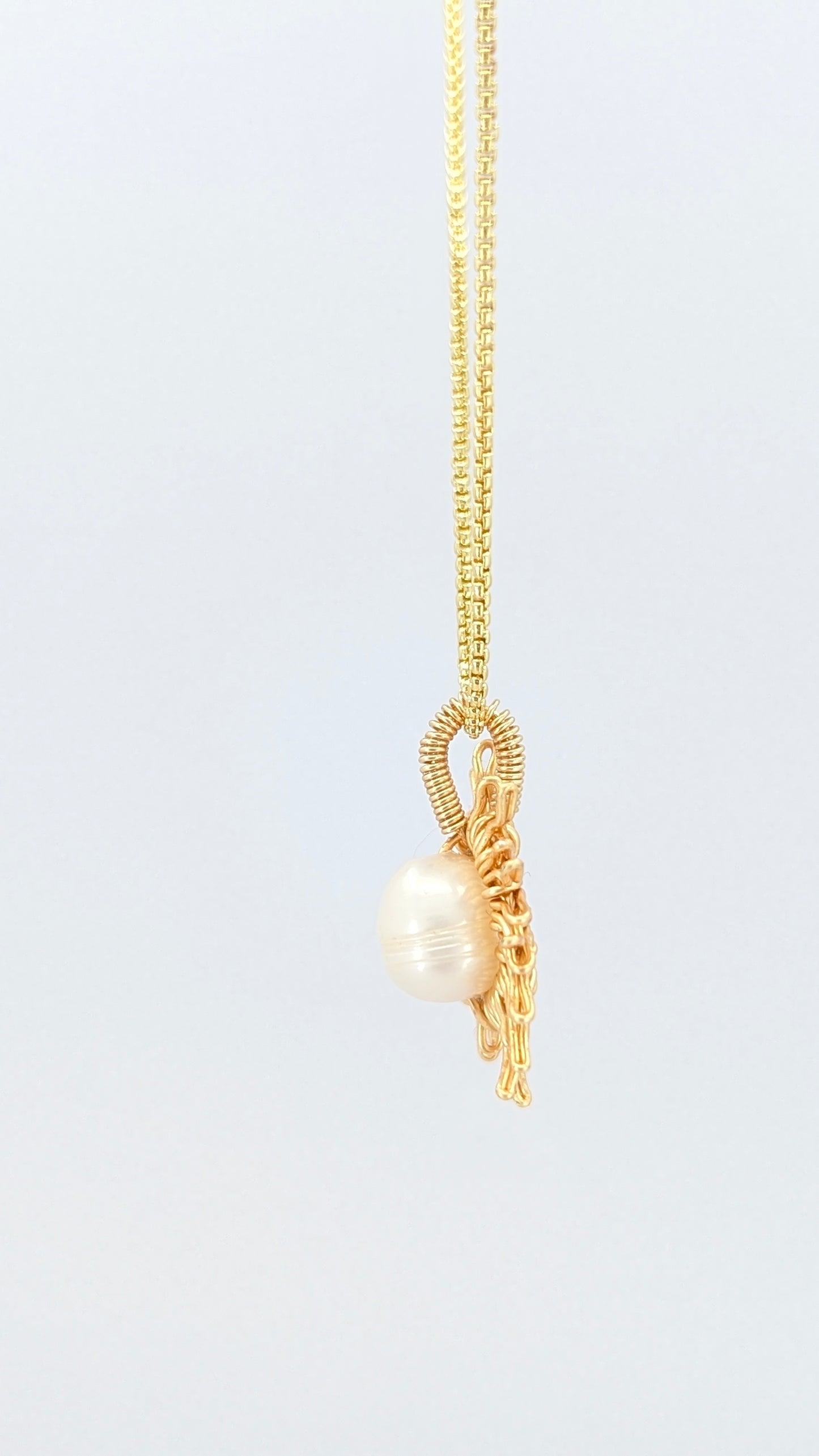 Lateral view of a gold necklace with a sun-shaped pendant featuring a pearl on a light gray background