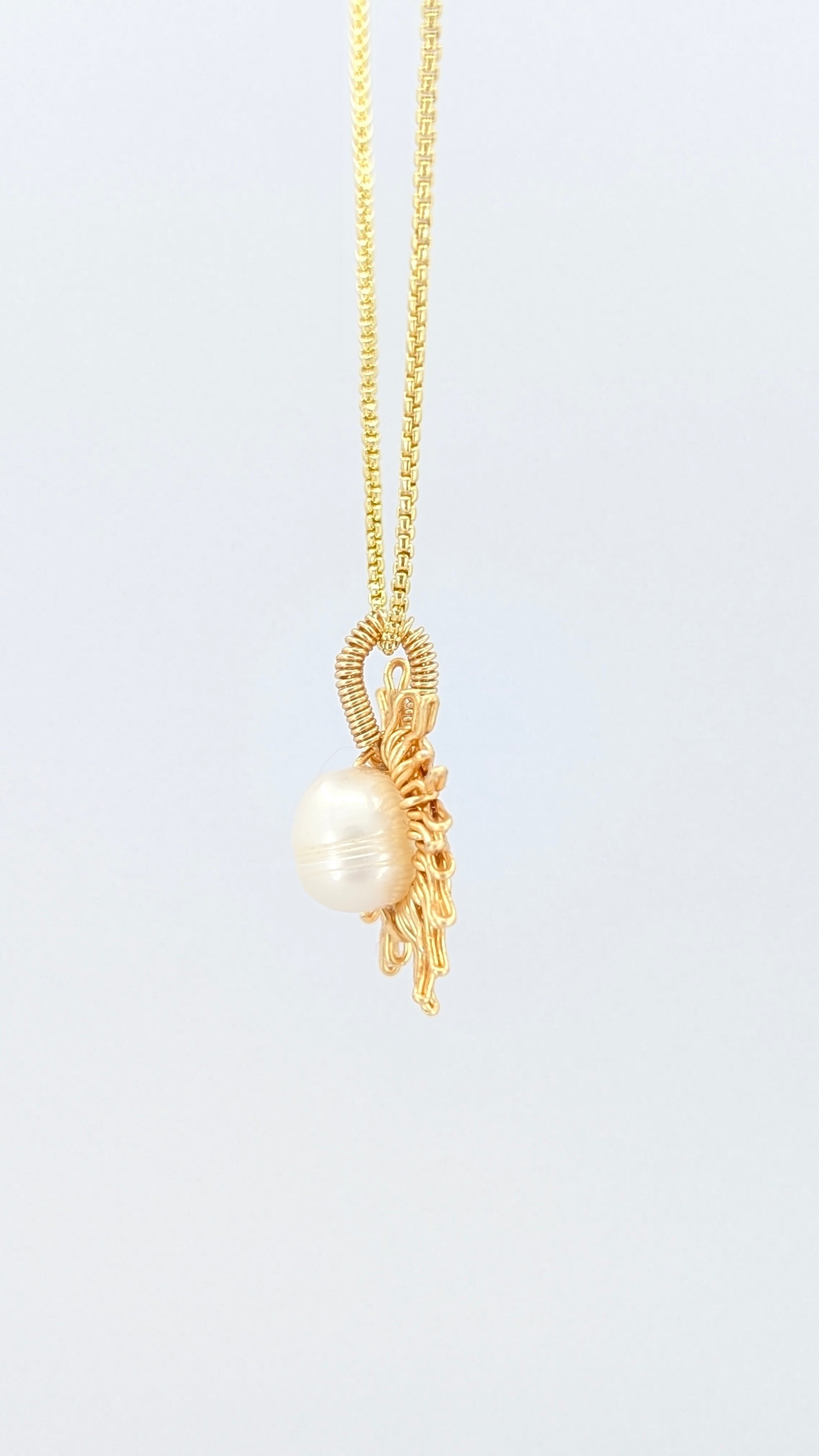 Lateral view of a gold necklace with a sun-shaped pendant featuring a pearl on a light gray background