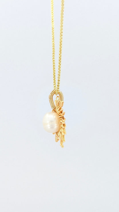 Lateral view of a gold necklace with a sun-shaped pendant featuring a pearl on a light gray background