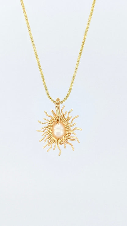 Back view of a gold necklace with a sun-shaped pendant featuring a pearl on a light gray background