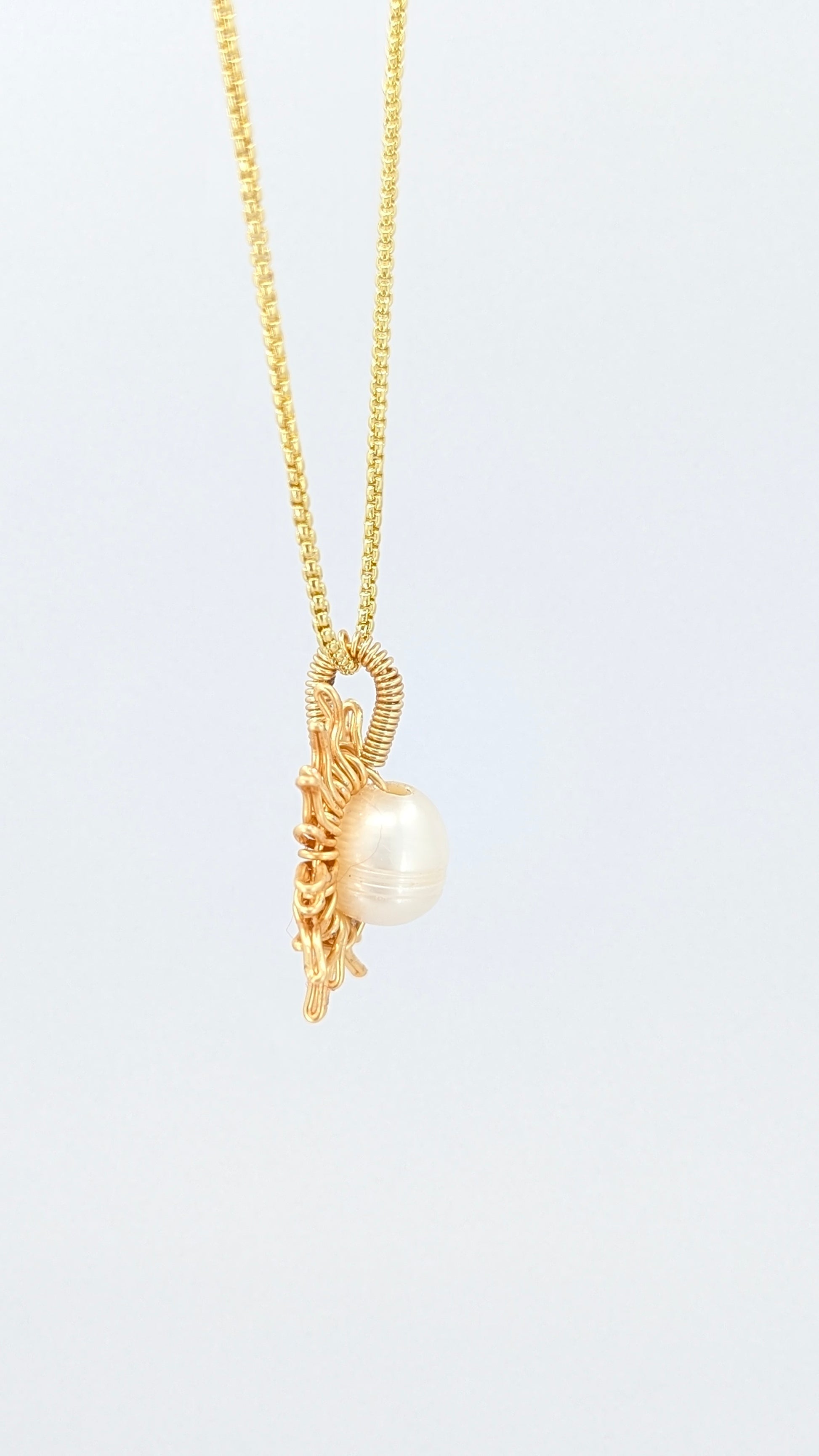 Lateral view of a gold necklace with a sun-shaped pendant featuring a pearl on a light gray background