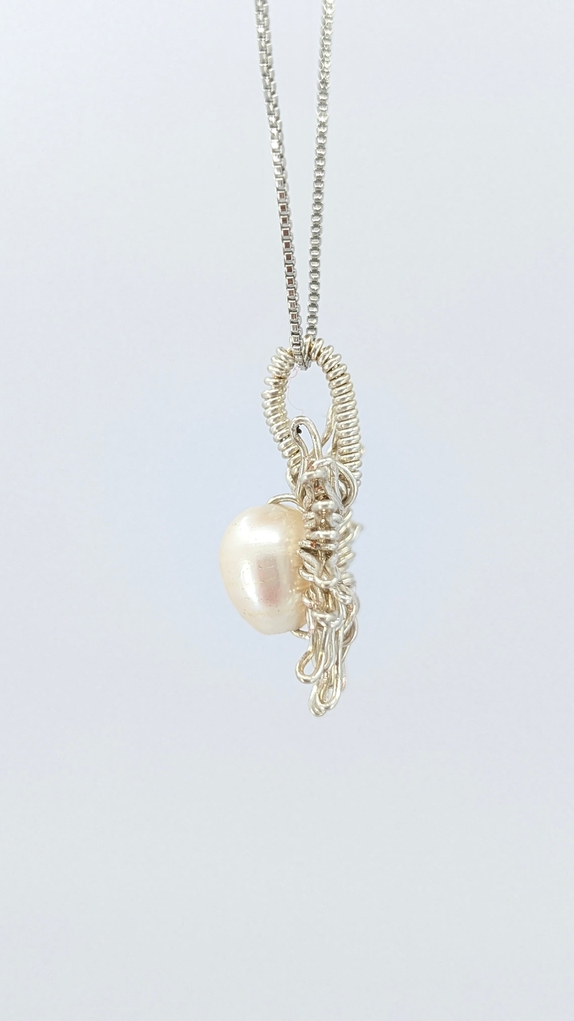 Lateral view of Necklace with a sun-shaped pendant featuring a freshwater pearl on a light gray background.