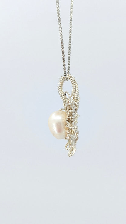Lateral view of Necklace with a sun-shaped pendant featuring a freshwater pearl on a light gray background.