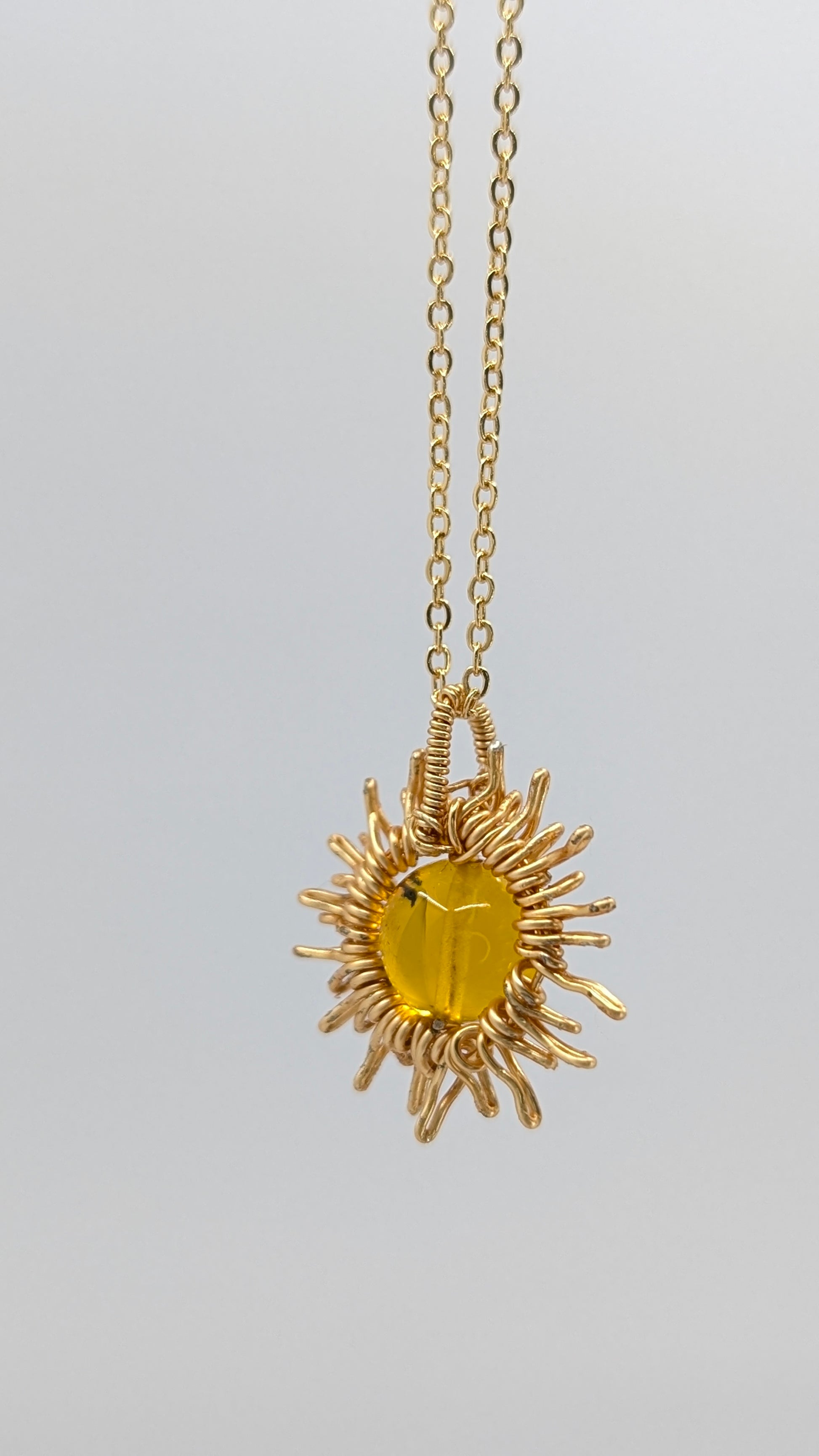 Handcrafted sun pendant necklace with warm rounded amber center stone on an adjustable gold-tone chain
