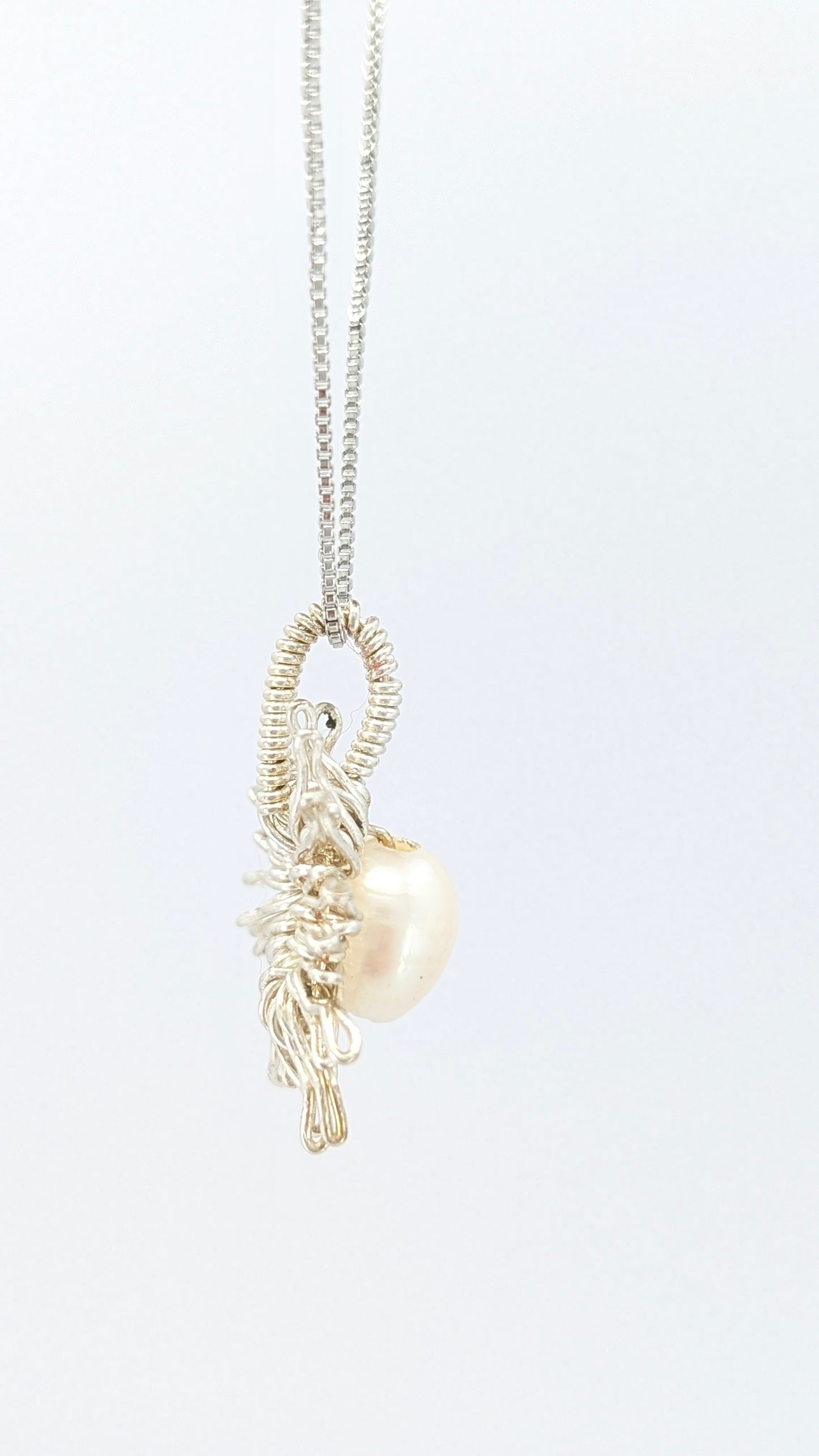 Lateral view of Necklace with a sun-shaped pendant featuring a freshwater pearl on a light gray background. Silver-plated chain and pendant.