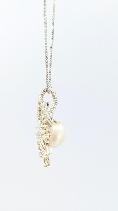 Lateral view of Necklace with a sun-shaped pendant featuring a freshwater pearl on a light gray background. Silver-plated chain and pendant.