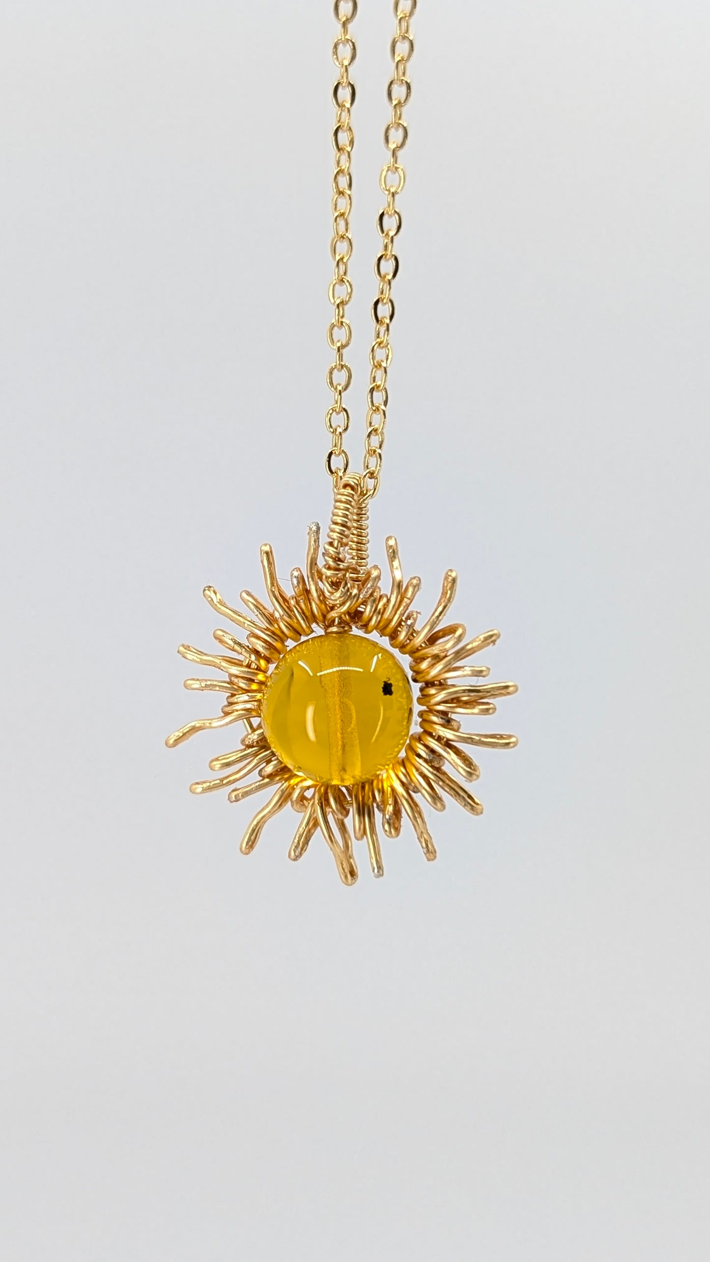 Handcrafted sun pendant necklace with warm rounded amber center stone on an adjustable gold-tone chain