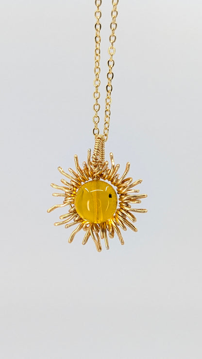Handcrafted sun pendant necklace with warm rounded amber center stone on an adjustable gold-tone chain