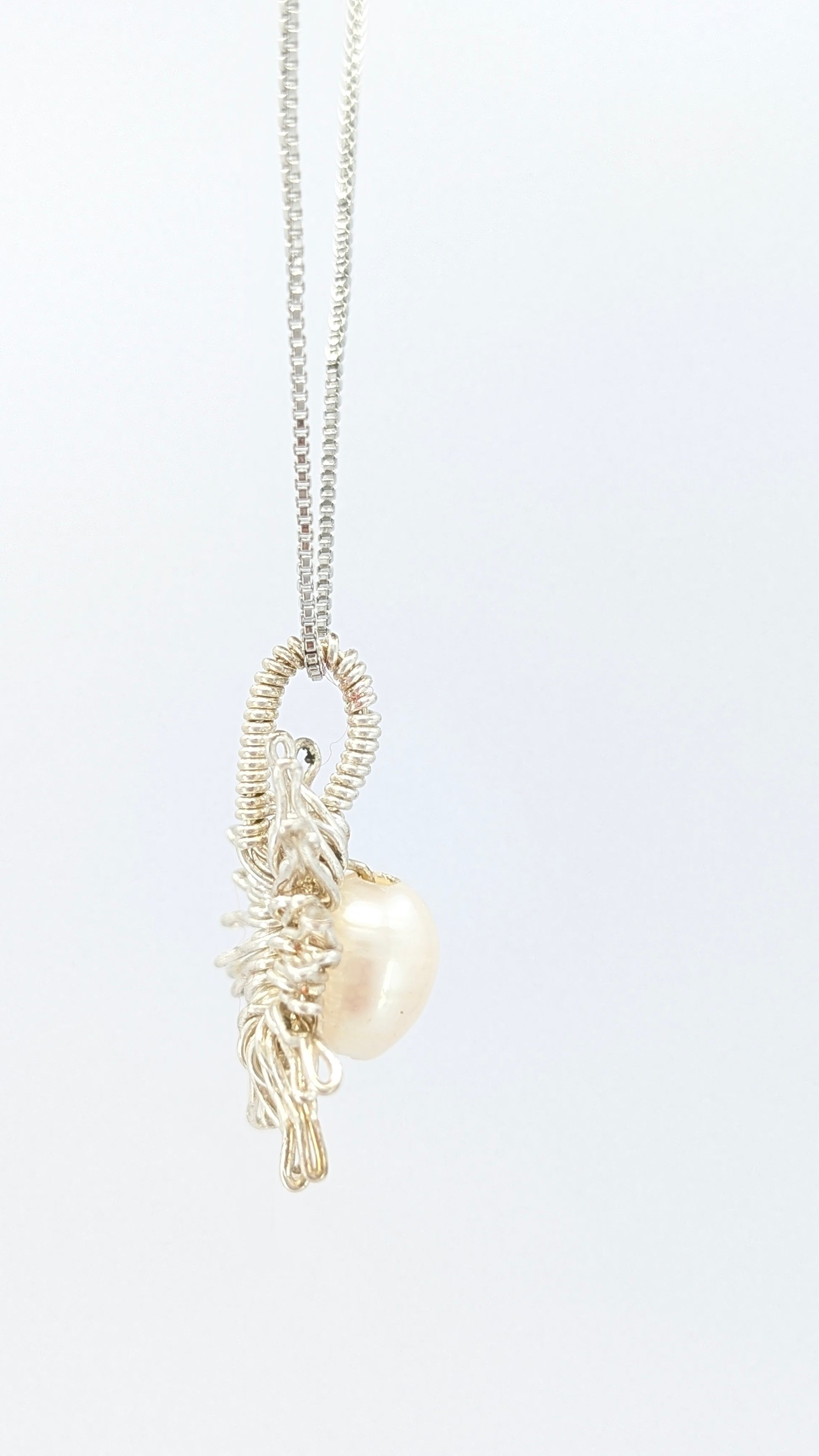 Lateral of Necklace with a sun-shaped pendant featuring a freshwater pearl on a light gray background.