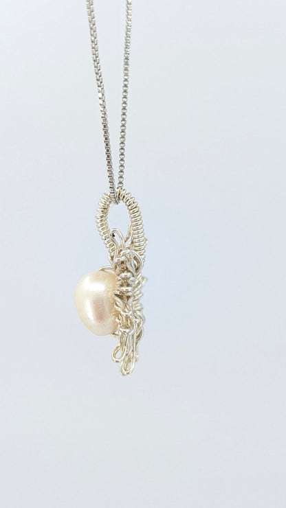 Lateral view of Necklace with a sun-shaped pendant featuring a freshwater pearl on a light gray background.