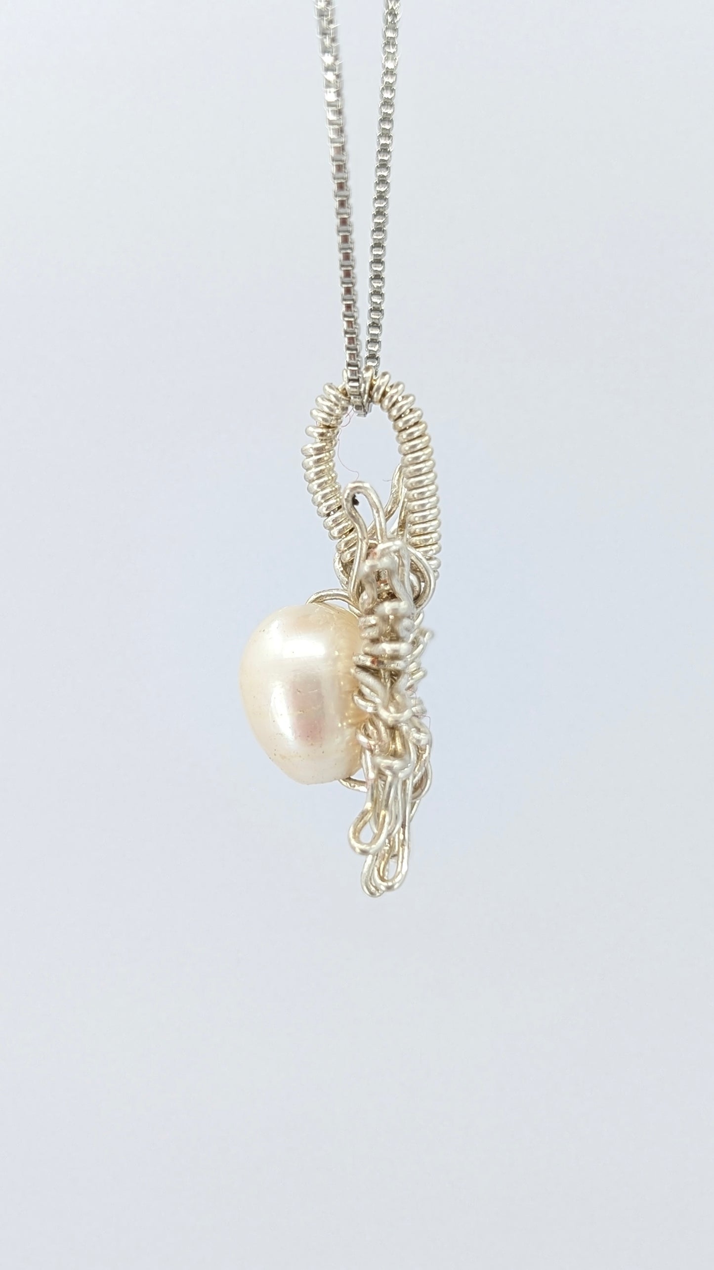 Another lateral  view of Necklace with a sun-shaped pendant featuring a freshwater pearl on a light gray background.