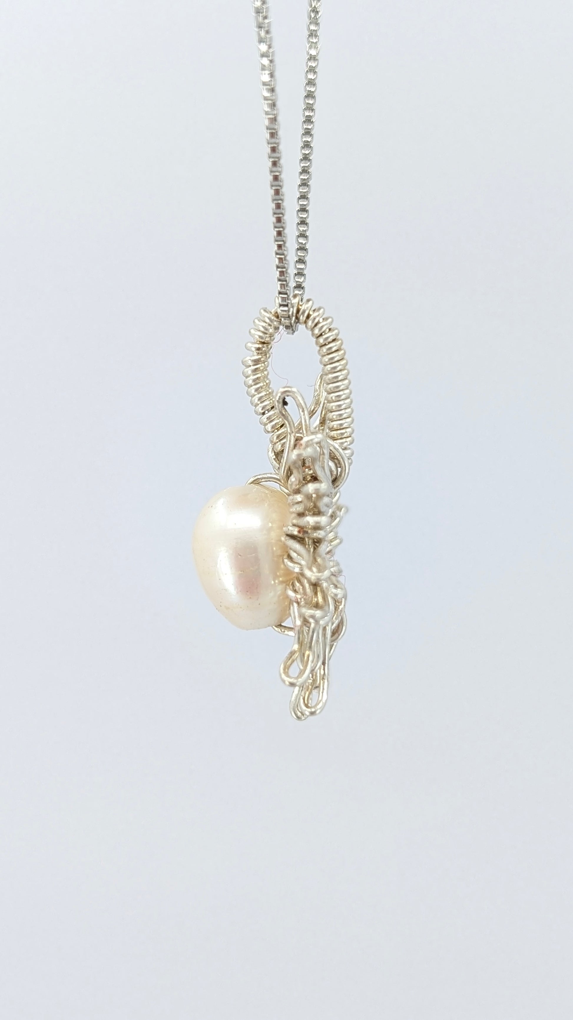 Another lateral  view of Necklace with a sun-shaped pendant featuring a freshwater pearl on a light gray background.